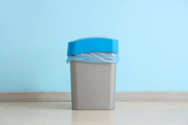 Mavi duvarın yanında çöp torbası olan bir çöp kutusu.