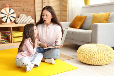 Female Asian speech therapist with laptop and little girl pronouncing letters in office