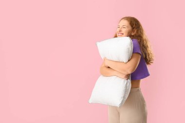 Pembe arka planda beyaz yumuşak yastıklı mutlu genç kadın