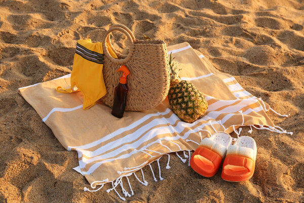 Stylish beach bag, flip-flops, pineapple, sunscreen spray, swimsuit and towel on sand