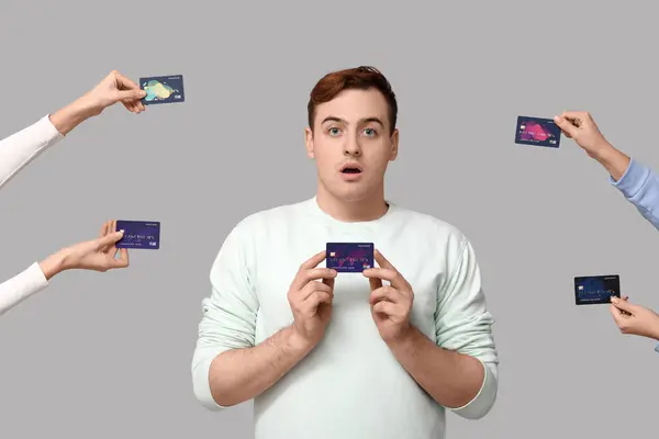 Schockierter Junger Mann Und Hände Mit Kreditkarten Auf Grauem Hintergrund — Stockfoto