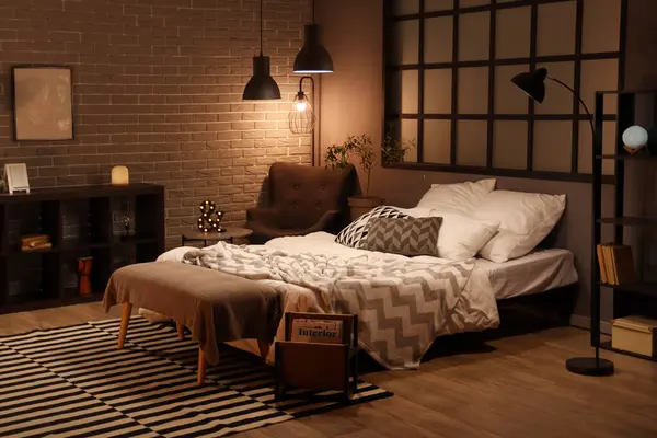 Interior of bedroom with blanket on bed and glowing lamps in evening