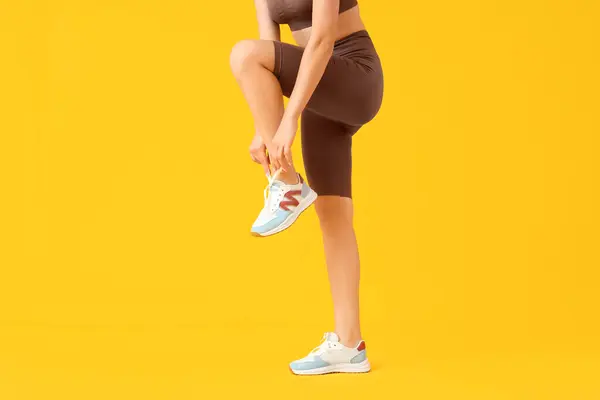 Young Woman Cycling Shorts Tying Shoe Laces Yellow Background — Stock Photo, Image