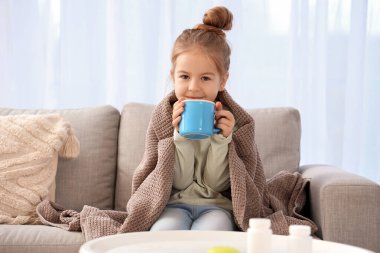 Hasta küçük kız evdeki kanepede çay içiyor.