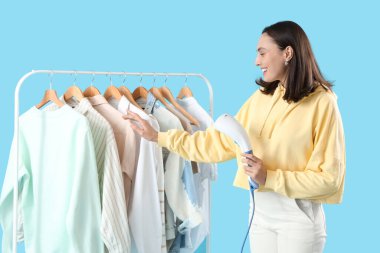 Modern buharlı ve mavi arka planda giysileri olan genç ve güzel bir kadın.