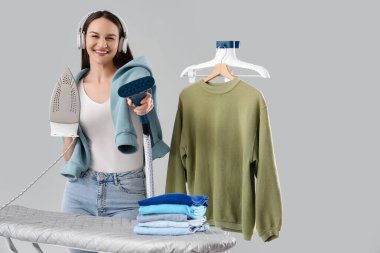 Demir ve giysi buharlı kulaklıklı güzel bir kadın gri arka planda müzik dinliyor.