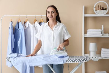 Çamaşır odasında giysileri ütüleyen güzel bir genç kadın.