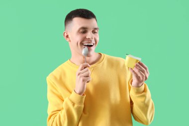 Lezzetli yoğurt ve yeşil arka planda kaşık olan genç adam.