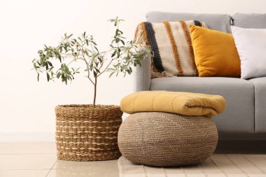 Beyaz duvarın yanında yastıklı, sedirli ve çiçekli şık gri kanepe.