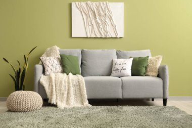 Yastıklı, sedirli ve yeşil duvarlı şık gri kanepe.