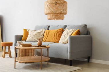 Yastıklı şık gri kanepe, sehpa ve sepet gri duvarın yanında.