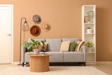 Kahve sehpası ve kahverengi duvarın yanında raf ünitesi olan şık gri kanepe.