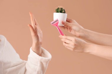 Güzel genç bir kadın, kahverengi arka planda tıraş bıçağını reddediyor.