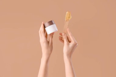 Kahverengi arka planda şekerleme macunu ve spatulası olan kadın eller konteynırı tutuyor