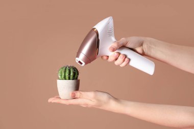 Kahverengi arka planda fotoepilator ve kaktüs olan kadın elleri.