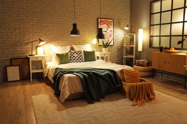 Rahat yatağın üzerinde battaniyeler ve gece lambaları olan modern yatak odasının içi.