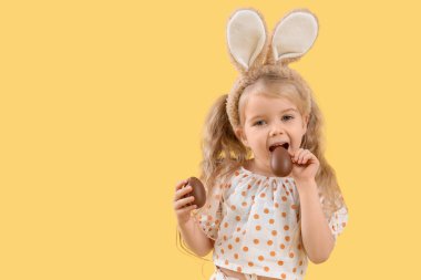 Tavşan kulaklı tatlı küçük kız ve sarı arka planda çikolatalı yumurtalar.