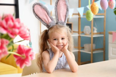 Dekorasyon odasındaki masada oturan tavşan kulaklı tatlı küçük kız. Paskalya kutlaması