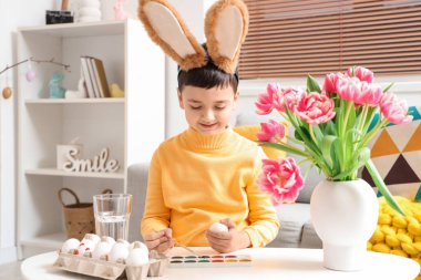 Tavşan kulaklı şirin çocuk evde paskalya yumurtası boyuyor.