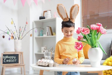 Tavşan kulaklı şirin çocuk evde paskalya yumurtası boyuyor.