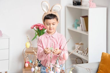 Tavşan kulaklı şirin çocuk evde söğüt dallarını paskalya yumurtasıyla süslüyor.