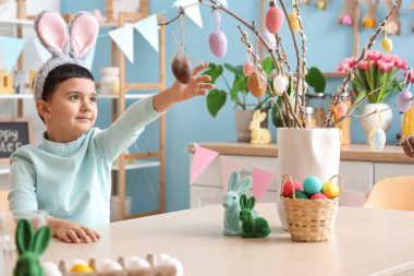 Tavşan kulaklı şirin çocuk evde söğüt dallarını paskalya yumurtasıyla süslüyor.