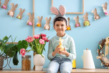Süslü mutfakta tezgahta oturan tavşan kulaklı ve oyuncak tavşanlı şirin bir çocuk. Paskalya kutlaması