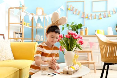 Tavşan kulaklı şirin çocuk evde paskalya yumurtası boyuyor.