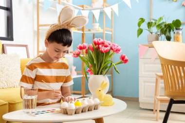 Tavşan kulaklı şirin çocuk evde paskalya yumurtası boyuyor.