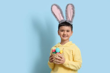 Mavi arka planda Paskalya yumurtaları olan tavşan kulaklı şirin bir çocuk.