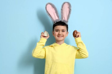 Mavi arka planda çikolata yumurtaları olan tavşan kulaklı şirin bir çocuk.