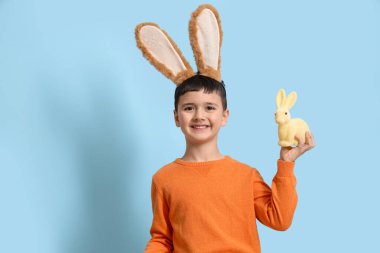 Mavi arka planda tavşan kulaklı ve oyuncak tavşanlı şirin bir çocuk. Paskalya kutlaması