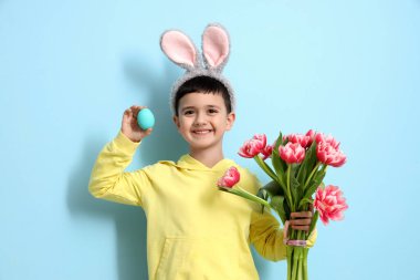Tavşan kulaklı şirin bir çocuk, lale çiçekleri ve mavi arka planda Paskalya yumurtası.