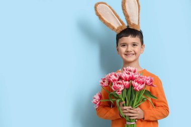 Tavşan kulaklı, mavi arka planda lale çiçekleri olan şirin bir çocuk. Paskalya kutlaması