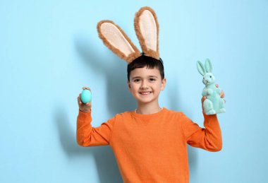 Tavşan kulaklı şirin bir çocuk, mavi arka planda paskalya yumurtası ve oyuncak tavşan.