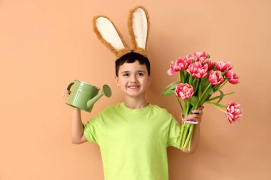 Tavşan kulaklı şirin bir çocuk, lale çiçekleri ve bej arka planda sulama kutusu. Paskalya kutlaması