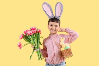 Tavşan kulaklı sevimli küçük çocuk, Paskalya yumurtaları ve lale çiçekleri ve sarı arka planda