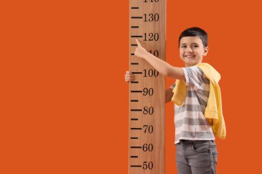 Turuncu arka planda tahta stadyumun yanında boyunu ölçen sevimli bir çocuk.