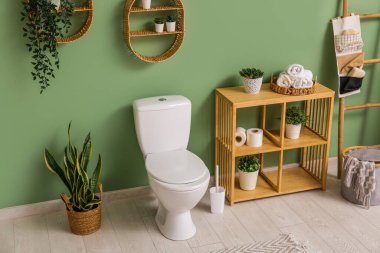 Yeşil duvarın yanında seramik klozeti olan şık bir banyo.