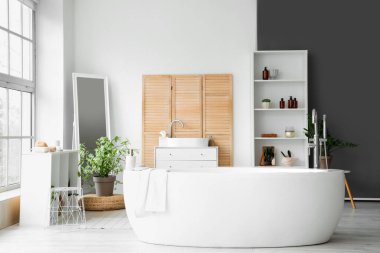 Geniş banyonun içinde panoramik pencereli beyaz küvet.