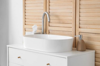 Seramik lavabo ve beyaz çekmeceler banyoda ahşap duvarın yanında.