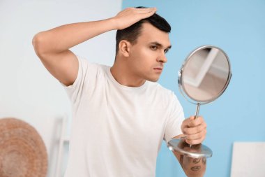 Saç dökülme sorunu olan genç adam aynaya bakıyor, yakın plan.