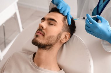 Genç adam hastanedeki kanepede saç uzatmak için iğne oluyor.