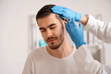 Alnı işaretli genç adam hastanede saç büyümesi için iğne oluyor, yakın plan.