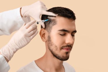 Genç adam bej arka planda saç büyümesi için iğne oluyor, yakın plan.