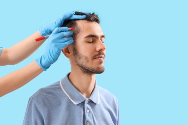 Doktor genç esmer adamın alnını mavi arka planda işaretliyor.