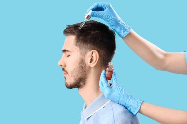 Genç esmer adam mavi arka planda saç uzaması tedavisi görüyor.