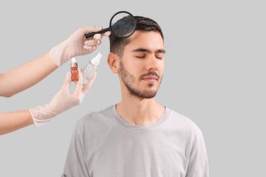 Saç büyütmek için ürünleri olan bir doktor genç adamın kafasını hafif arka planda inceliyor, yakın plan.