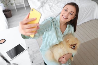 Pomeranya köpeği olan genç bir kadın yatak odasında selfie çekiyor.