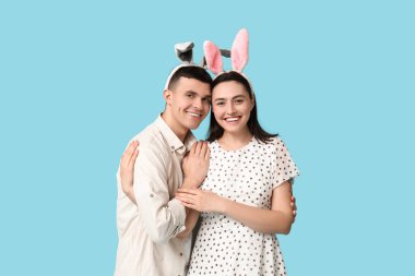 Mavi arka planda Paskalya tavşanı kulakları olan mutlu genç çift